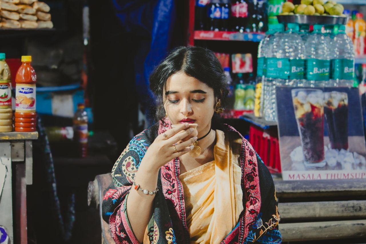 The Art of Drawing Readers In: Your attractive post title goes here A woman in a saree enjoys tea at a bustling Indian street market, surrounded by vibrant colors.